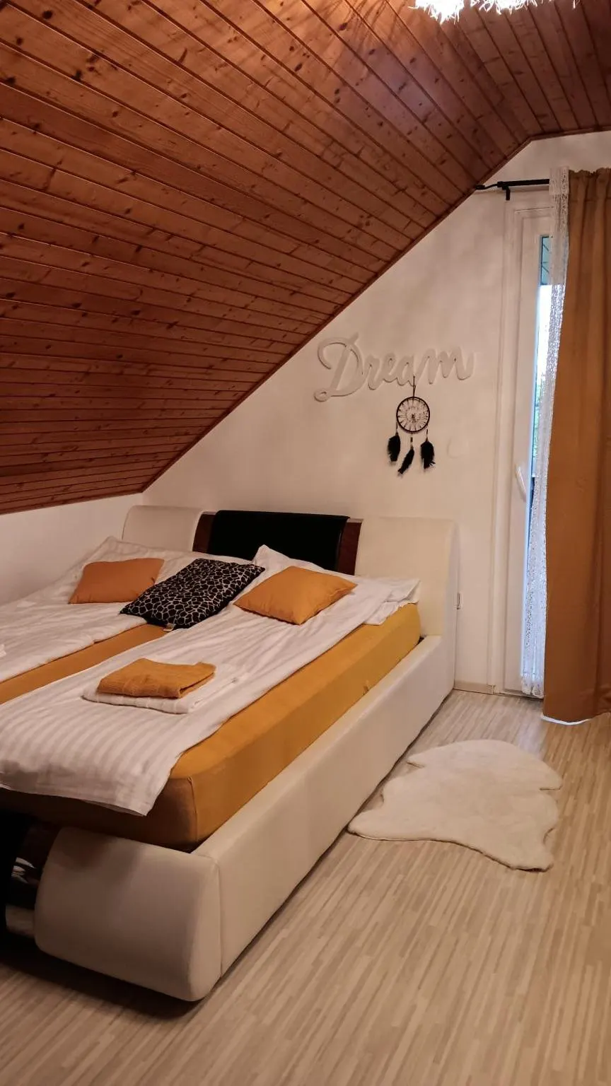 Spalnica pod poševnim lesenim stropom z veliko zakonsko posteljo